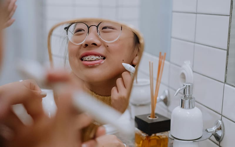 A teen girl looking at her braces in a mirror